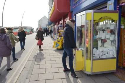 Man playing on a grabber machine filled with rolls of toilet paper