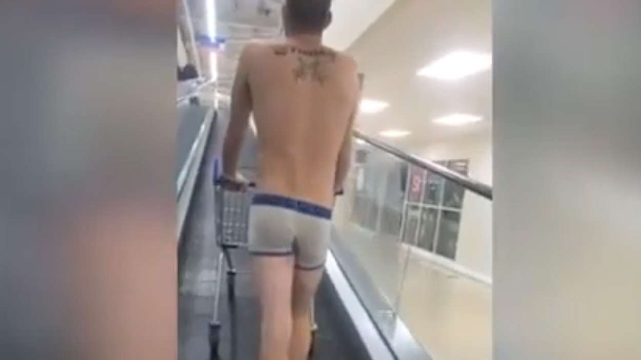 Man just wearing pants walking into supermarket